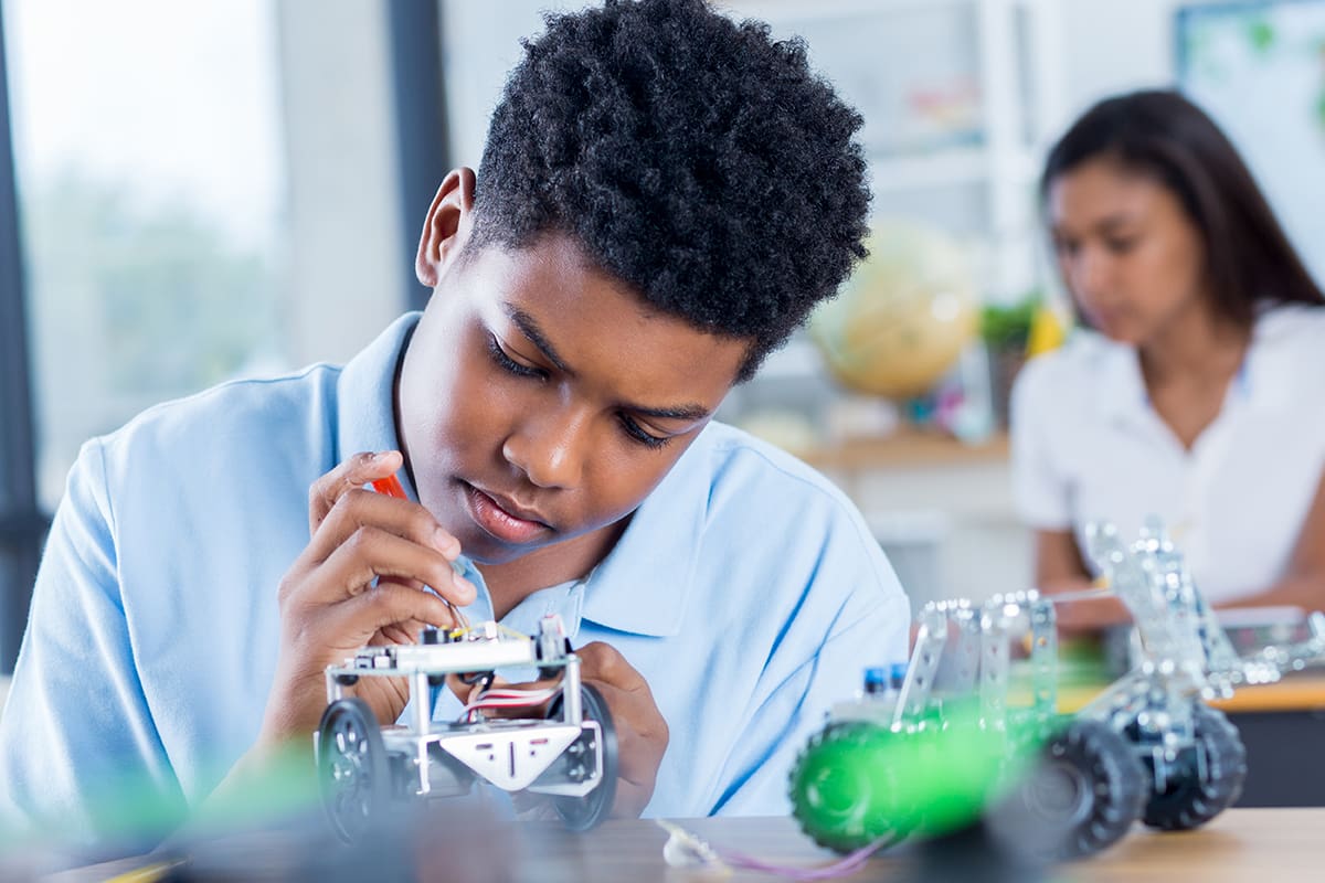 Teen boy working on a robot with a screwdriver 